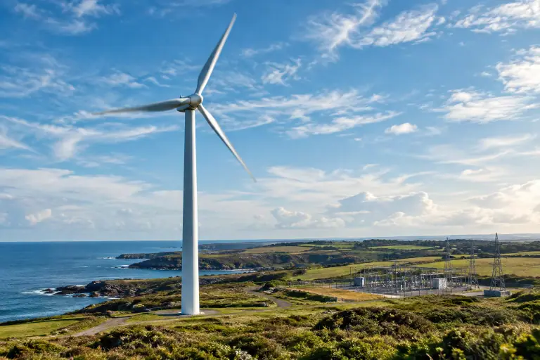 Une éolienne domine un cap français près d’un poste électrique discret.
